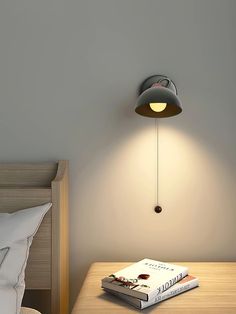 a book is sitting on top of a bed next to a lamp that's attached to the wall