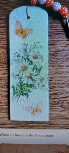 a wooden bookmark with flowers and butterflies on it, next to a beaded bracelet