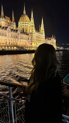 a woman is looking out over the water in front of a large building at night