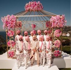 a group of men standing next to each other in front of a gazebo with pink flowers on it