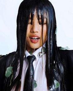 a woman with long black hair wearing a suit and tie, covered in fake flowers