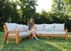 a woman sitting on top of a wooden couch in the middle of a grass field