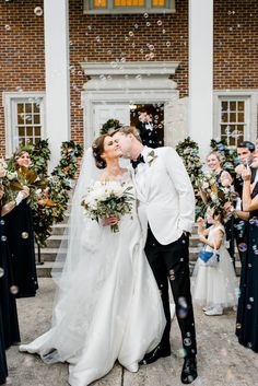 a newly married couple kissing in front of their wedding party with bubbles coming from them