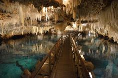 a wooden walkway leads to an underground cave with stalate formations and blue water