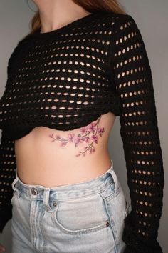 a woman with a flower tattoo on her stomach, wearing jeans and a black crop top