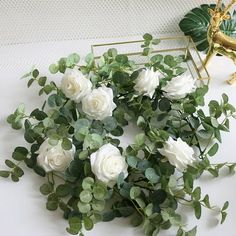 white roses and green leaves are arranged on a table next to a gold statue,