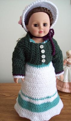 a crocheted doll wearing a green and white dress on a wooden table next to a figurine