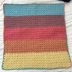 a multicolored crocheted blanket sitting on top of a bed next to a ball of yarn