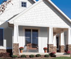 a white house with two wooden benches on the front porch and flowers in pots next to it