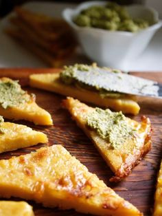 several slices of pizza on a wooden cutting board with pesto and cheese toppings