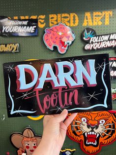 a person holding up a sign that says darn tofuin in front of a wall covered with stickers