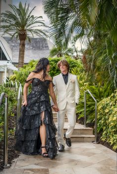 two people dressed in formal wear walking down the stairs together with palm trees behind them