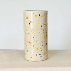 a white vase with multicolored dots on it sitting on a table top next to a wall