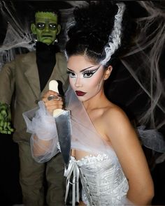 a woman dressed in white holding a knife next to a man with green makeup on his face