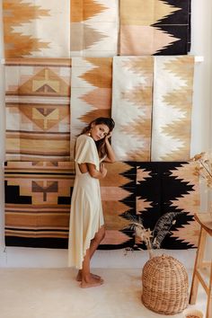 a woman standing in front of several rugs on the wall with her hands to her face