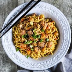 a white bowl filled with noodles and meat on top of a wooden table next to chopsticks