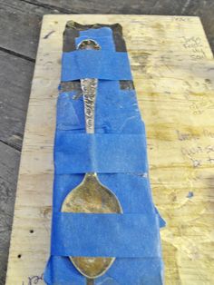 a wooden table topped with blue tape and a metal spoon on top of it's side