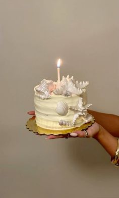 a person holding a cake with a lit candle on it and seashells all over it