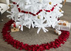 a white christmas tree with red and gold ornaments on it, surrounded by other presents