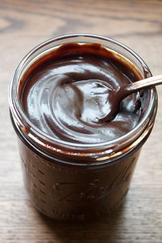 a jar filled with chocolate pudding on top of a wooden table next to a spoon