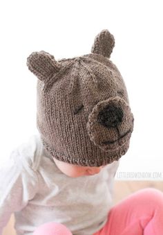 a baby wearing a knitted bear hat sitting on top of a wooden floor in front of a white wall