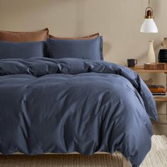 a bed with blue comforter and pillows in a living room next to a lamp