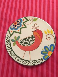 a plate with a bird painted on it sitting on a pink and white table cloth