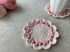 two crocheted coasters sitting on top of a table next to a white vase