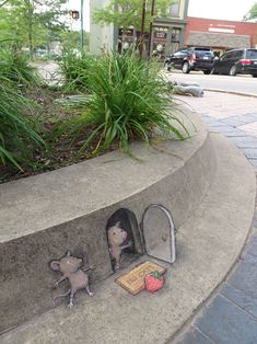 two mice in a mailbox on the side of a sidewalk with grass and bushes