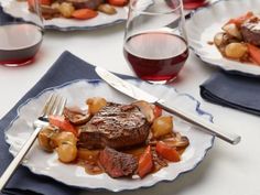 a plate with steak, potatoes and carrots on it next to some wine glasses