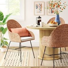 two wicker chairs and a round table in a white room with potted plants