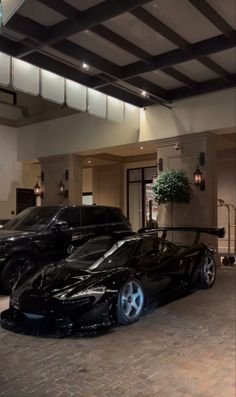 two black sports cars parked in front of a hotel lobby with potted plants on the roof