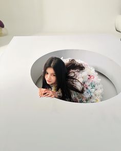 a woman is sitting in a white box with flowers on the floor and her hair blowing in the wind