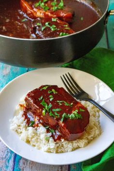 a white plate topped with rice and meat next to a pot of chili sauce on a table