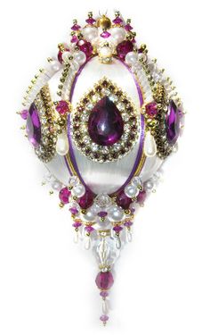 a purple and white brooch with pearls on it's sides, surrounded by other beads