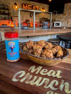 a wooden table topped with a bowl of meatballs next to a bottle of sauce