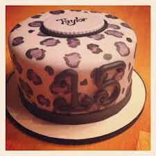 a birthday cake decorated with purple and black leopard print on a white plate, sitting on a wooden table