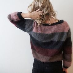 a woman standing in front of a wall with her hands on her head while wearing a striped sweater