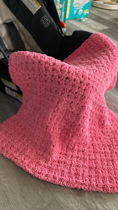 a pink crocheted seat cover sits on the floor next to a stroller