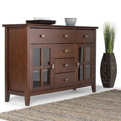 a large wooden cabinet sitting on top of a rug next to a vase with grass in it