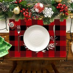 a christmas table setting with red and black buffalo plaid placemats, silverware and evergreen branches