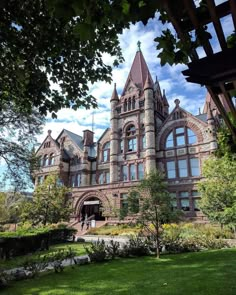 an old brick building with many windows on the front and side of it, surrounded by lush green grass