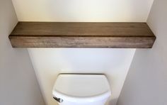 a white toilet sitting in a bathroom next to a wooden shelf above it's tank