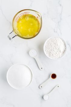 ingredients to make homemade cake on white marble counter top with measuring spoons and measuring cup