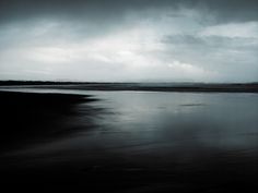 a black and white photo of a body of water under a dark sky with clouds