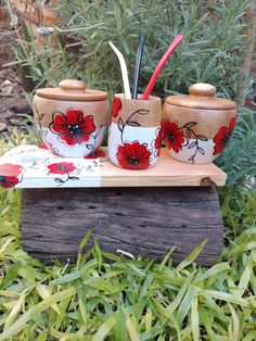 three red flowers painted on white ceramic cups and spoons sitting on a wooden stand