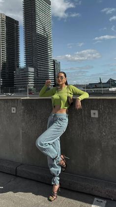 a woman leaning against a wall in front of tall buildings