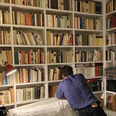 a person sitting on a bed in front of a book shelf