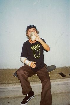 a man sitting on top of a skateboard while drinking from a cup in his hand