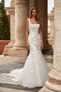 a woman standing in front of columns wearing a white dress with floral appliques